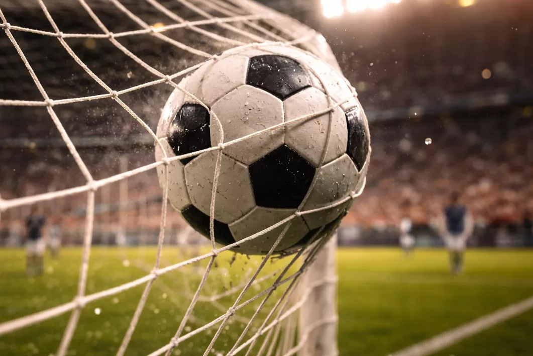 Red de portería de fútbol con el balón entrando durante un gol en un estadio iluminado